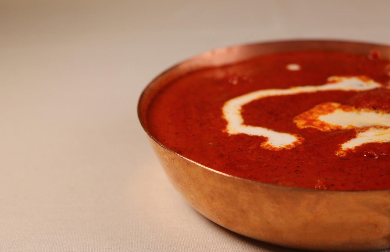 Close up of a metal serving bowl of curry swirled with cream